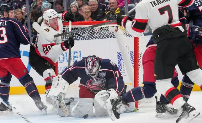 Columbus Blue Jackets goaltender Jet Greaves (73) covers the puck between Ottawa Senators left wing Fabian Zetterlund (20) and left wing Brady Tkachuk (7) in the second period of an NHL hockey game Thursday, Dec. 11, 2025, in Columbus, Ohio. (AP Photo/Sue Ogrocki)