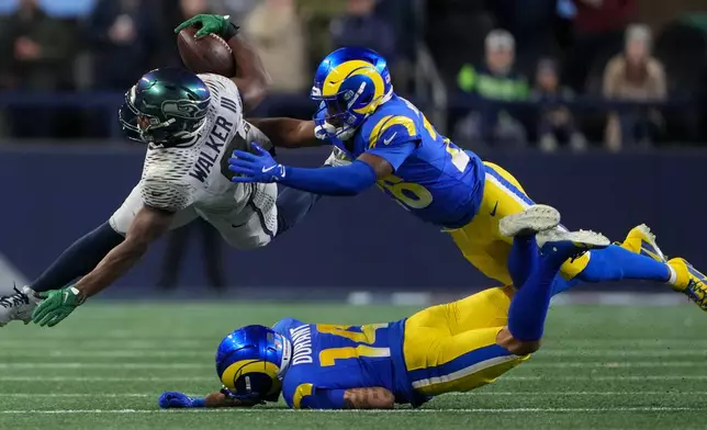 Seattle Seahawks running back Kenneth Walker III (9) tries to get past Los Angeles Rams safety Kamren Kinchens, right, cornerback Cobie Durant (14) during the first half of an NFL football game Thursday, Dec. 18, 2025, in Seattle. (AP Photo/Lindsey Wasson)