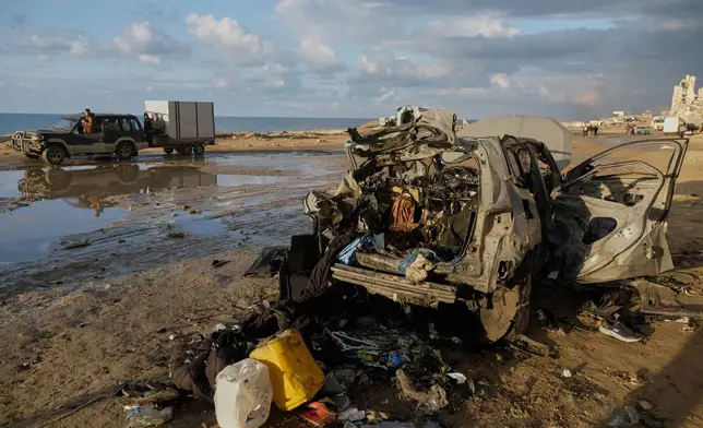 Palestinians drive past a destroyed car following an Israeli strike in Gaza City, Saturday, Dec. 13, 2025. (AP Photo/Jehad Alshrafi)