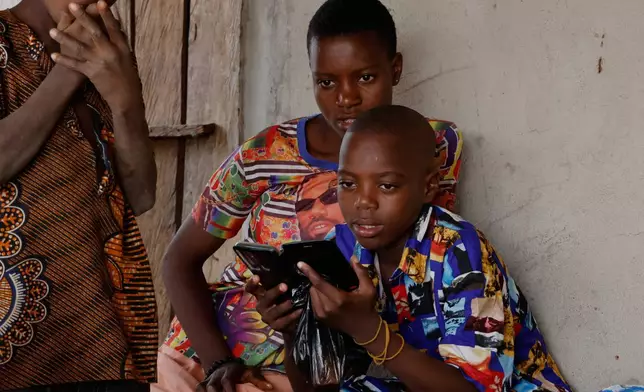Onyeka Chieme, right, a student of St. Mary's Catholic School, who was abducted by gunmen and later released, checks a mobile phone in his house in Papiri, Nigeria, Wednesday, Dec. 10, 2025. (AP Photo/Afolabi Sotunde)