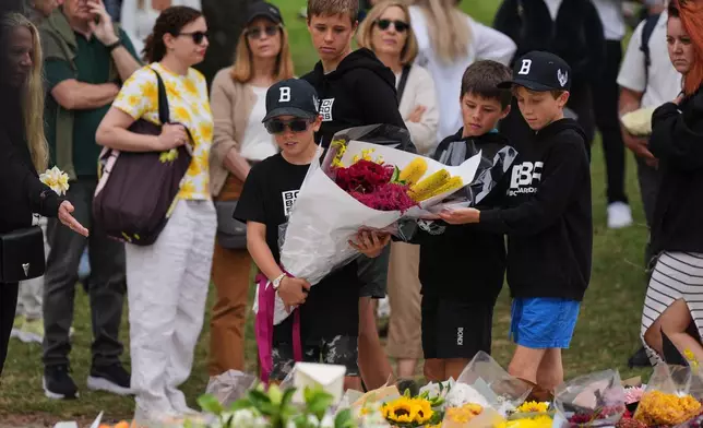 Boys lay flowers at a flower memorial for victims of Sunday's shooting at the Bondi Pavilion at Bondi Beach on Tuesday, Dec. 16, 2025, in Sydney, Australia. (AP Photo/Mark Baker)