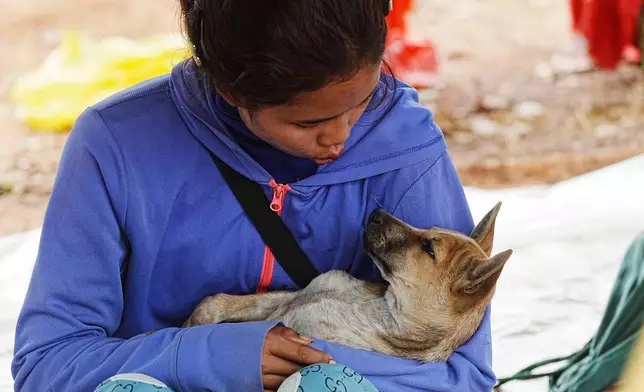 A woman plays with a dog as she takes refuge at Chonkal district in Oddar Meanchey province, Cambodia Thursday, Dec. 11, 2025, after fleeing from home following a fighting between Thailand and Cambodia over territorial claims. (AP Photo/Heng Sinith)