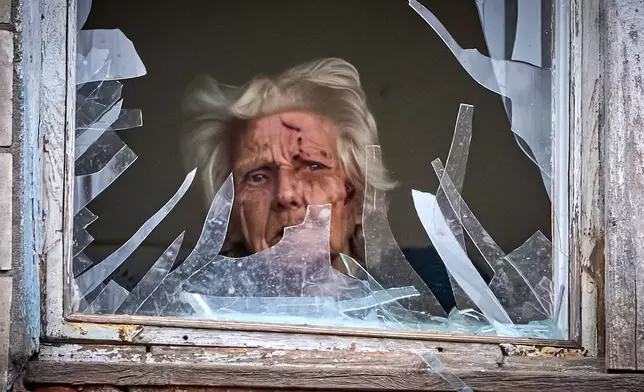 An injured elderly woman looks out of her broken window as an apartment building was hit by a Russian drone during an aerial attack in Kyiv, Ukraine, Tuesday, Dec. 23, 2025. (AP Photo/Efrem Lukatsky)