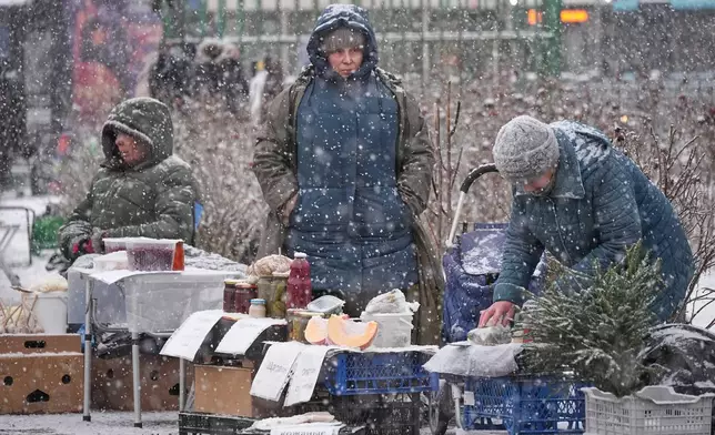 Women sell foodstuffs at a spontaneous market near a subway station during snowfall in St. Petersburg, Russia, Tuesday, Dec. 23, 2025. (AP Photo/Dmitri Lovetsky)