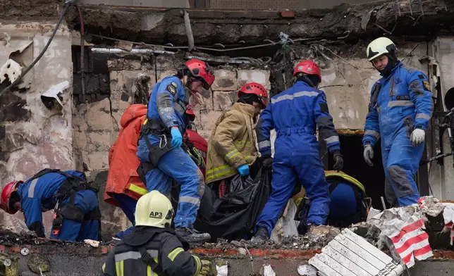 Rescuers carry the body of a victim after Russian drone hit a multi-storey apartment building during a massive missile and drone attack in Kyiv, Ukraine, Saturday, Dec. 27, 2025. (AP Photo/Efrem Lukatsky)