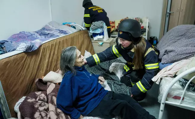 A psychologist of a rescue team helps en elderly woman at the hospice which was damaged after a Russian strike on Kyiv, Ukraine, on Saturday, Dec. 27, 2025. (AP Photo/Evgeniy Maloletka)