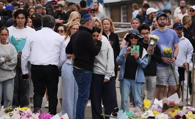 People offer flowers and hugs at a floral memorial during a tribute for victims of Sunday's shooting at the Bondi Pavilion at Bondi Beach on Tuesday, Dec. 16, 2025, in Sydney, Australia. (AP Photo/Mark Baker)