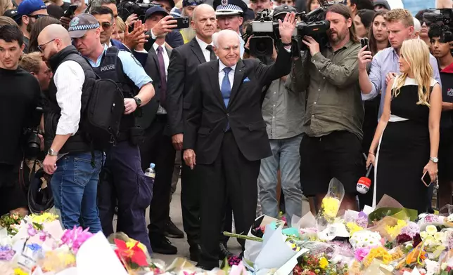 Former PM John Howard waves during a flower memorial for victims of Sunday's shooting at the Bondi Pavilion at Bondi Beach on Tuesday, Dec. 16, 2025, in Sydney, Australia. (AP Photo/Mark Baker)