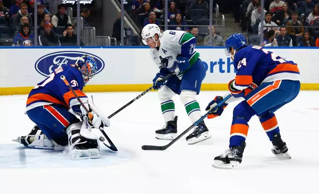 New York Islanders goaltender Ilya Sorokin, left, makes a save against Vancouver Canucks right wing Brock Boeser (6) during the first period of an NHL hockey game, Friday, Dec. 19, 2025, in Elmont, N.Y. (AP Photo/Noah K. Murray)