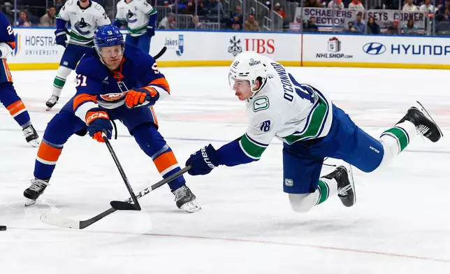 Vancouver Canucks left wing Drew O'Connor (18) shoots against New York Islanders Emil Heineman (51) during the first period of an NHL hockey game, Friday, Dec. 19, 2025, in Elmont, N.Y. (AP Photo/Noah K. Murray)