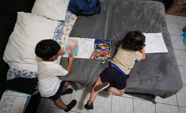 Jakelin Pasedo's sons, ages 5 and 3, color on the bed inside the Miami-area motel room where the trio live, all of whom have refugee status, Wednesday, Oct. 22, 2025, after their father requested to be sent back to Venezuela after months in immigration detention. (AP Photo/Rebecca Blackwell)