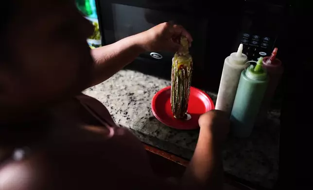 Guatemalan migrant Amavilia, 31, shows how she prepares the corn-on-the-cob she sells, inside her South Florida apartment, Wednesday, Oct. 8, 2025, after her infant son's father, who worked in construction, was detained and deported to Guatemala. (AP Photo/Rebecca Blackwell)