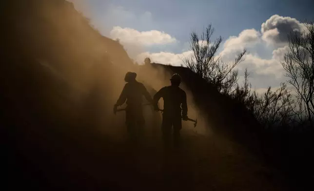 Members of the Navajo Scouts firefighter crew kick up dust as they clear debris from a landslide across a road on a hillside as they battle the Eaton Fire, Jan. 17, 2025, in Altadena, Calif. (AP Photo/John Locher, File)