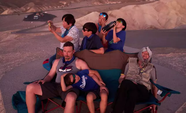 Joe Chyuwei, right, Addison Black, front center, James Black, front left, and back row from left, Helen Chyuwei, Jameson Black, Grace Chyuwei and Grayson Black watch the sunset in the heat at Zabriskie Point, Aug. 3, 2025, in Death Valley National Park, Calif. (AP Photo/John Locher, File)