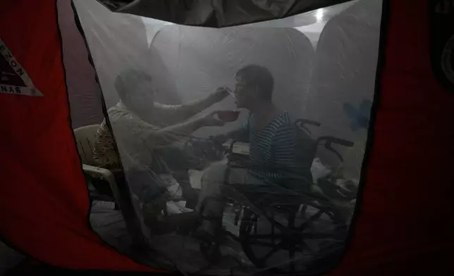 Judy Bertuso, left, feeds her husband Apollo inside a tent at an evacuation center as Typhoon Fung-wong enters the country Nov. 9, 2025, in Quezon city, Philippines. (AP Photo/Aaron Favila, File)