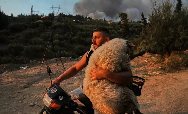 Olsjen Mucobega, 32, uses his motorcycle to evacuate a sheep from a wildfire Aug. 13, 2025, in Patras, Greece. (AP Photo/Thanassis Stavrakis, File)