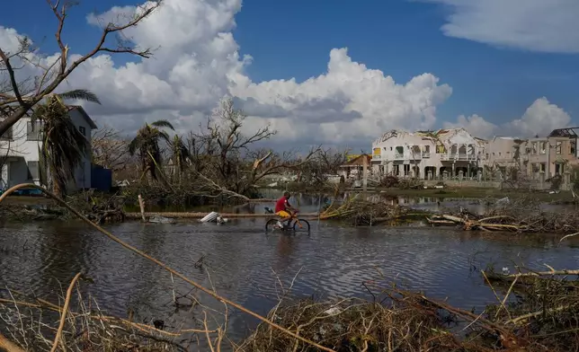 A man rides his bicycle through an inundated street during the aftermath of Hurricane Melissa, Oct. 30, 2025, in Black River, Jamaica. (AP Photo/Matias Delacroix, File)