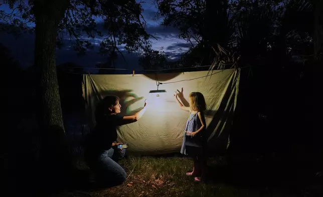 Schuyler Clogston, left, makes shadows puppets with Agnes Suárez after setting up a sheet and light to attract moths for observation Oct. 7, 2025, in Charleston, S.C. (AP Photo/Joshua A. Bickel, File)
