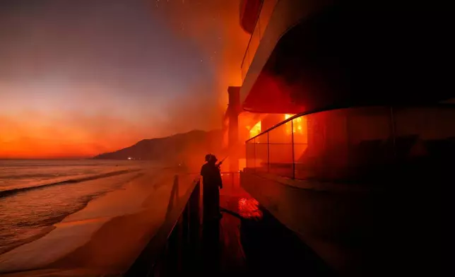 Firefighters work from a deck as the Palisades Fire burns a beachfront property Jan. 8, 2025, in Malibu, Calif. (AP Photo/Etienne Laurent, File)