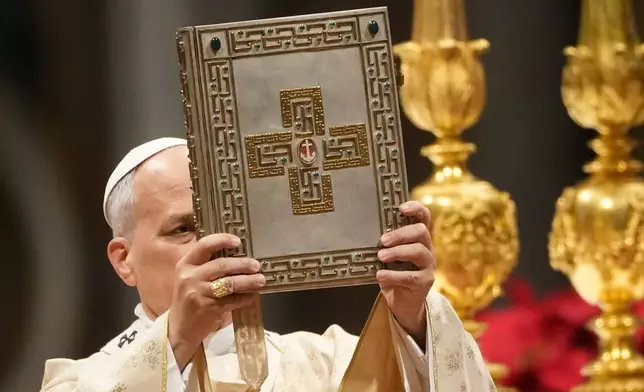 Pope Leo XIV holds up the book of the Gospel during the Christmas Day Mass at the St. Peter's Basilica at the Vatican, Thursday, Dec. 25, 2025. (AP Photo/Gregorio Borgia)