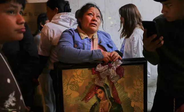 A woman cries as she looks up at the Virgin of Guadalupe image handing on the wall at the Basilica of Our Lady of Guadalupe in Mexico City, on her feast day, Friday, Dec. 12, 2025. (AP Photo/Claudia Rosel)