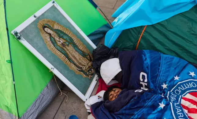 A pilgrim sleeps next to framed image of the Virgin of Guadalupe outside the Basilica of Guadalupe, in Mexico City, Thursday, Dec. 11, 2025, the day before her feast day. (AP Photo/Claudia Rosel)