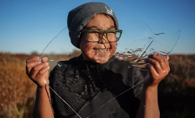 Charles Gallahorn, 10, plays with a slab of ice taken from a pond that formed on a warped road caused by thawing permafrost in Kotzebue, Alaska, Friday, Sept. 26, 2025. (AP Photo/Annika Hammerschlag)