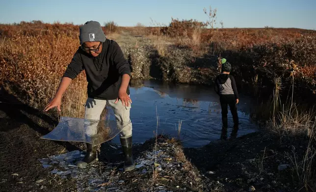 Charles Gallahorn, 10, plays with a slab of ice taken from a pond that formed on a warped road caused by thawing permafrost in Kotzebue, Alaska, Friday, Sept. 26, 2025. (AP Photo/Annika Hammerschlag)