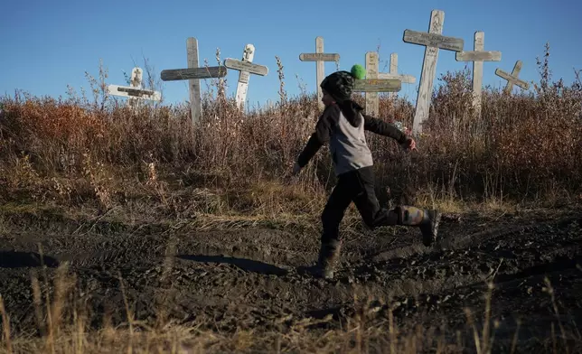 James Schaeffer, 7, runs through a cemetery where thawing permafrost has caused grave markers to tilt and the ground to warp in Kotzebue, Alaska, Friday, Sept. 26, 2025. (AP Photo/Annika Hammerschlag)