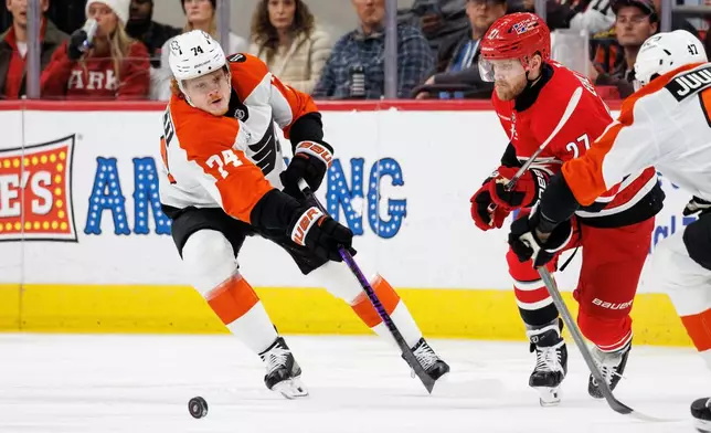 Philadelphia Flyers' Owen Tippett (74) sends the puck down the ice ahead of Carolina Hurricanes' Nikolaj Ehlers, center, during the second period of an NHL hockey game in Raleigh, N.C., Sunday, Dec. 14, 2025. (AP Photo/Ben McKeown)