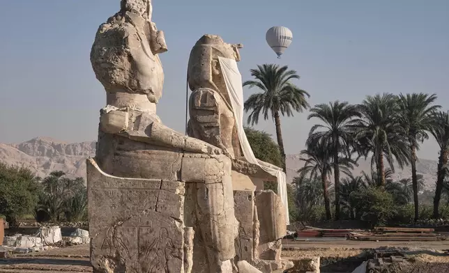 A hot air ballon flys over the assembly of two giant alabaster statues for Pharoah Amenhotep III, before the official opening, in the southern city of Luxor, Egypt, Sunday, Dec. 14, 2025. (AP Photo/Amr Nabil)