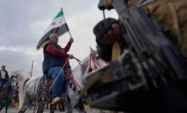 A Syrian man rides his horse and waves his country flag during celebrations marking the first anniversary of the ousting of former President Bashar Assad in Damascus, Syria, Monday, Dec. 8, 2025. (AP Photo/Hussein Malla)