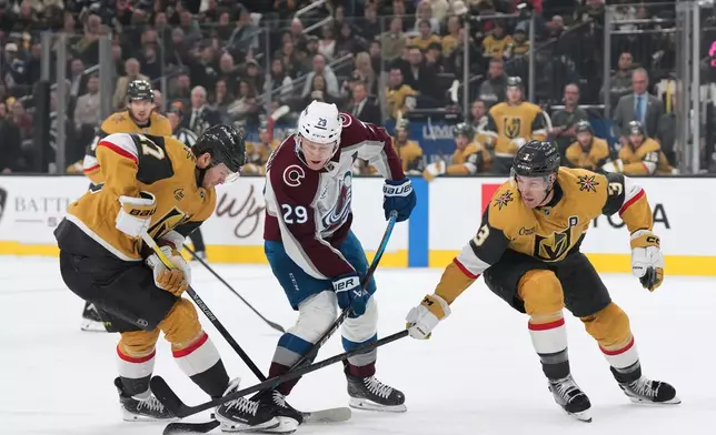 Colorado Avalanche center Nathan MacKinnon (29) skates with the puck against Vegas Golden Knights defensemen Ben Hutton, left, and Brayden McNabb (3) during the first period of an NHL hockey game, Saturday, Dec. 27, 2025, in Las Vegas. (AP Photo/Candice Ward)