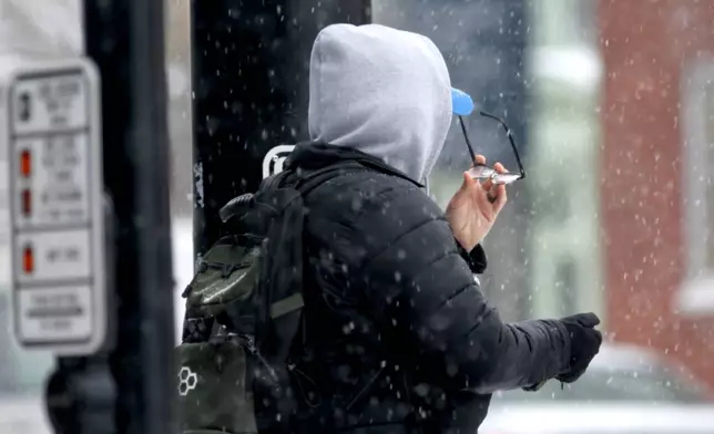 A person checks their glasses as it snows in Portsmouth, N.H., Tuesday, Dec. 2, 2025. (AP Photo/Caleb Jones)