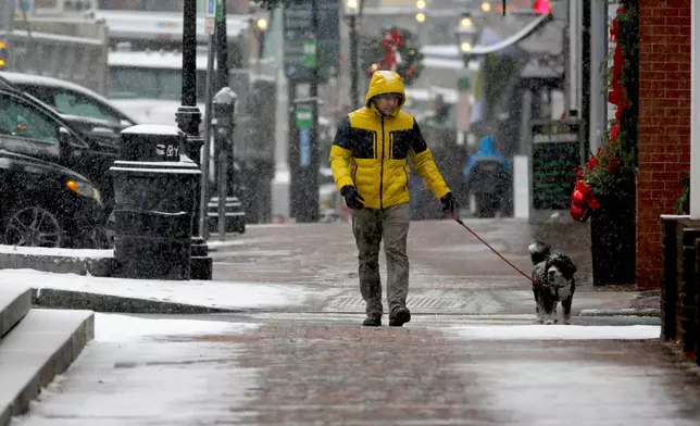 A person walks a dog in the snow in Portsmouth, N.H., Tuesday, Dec. 2, 2025. (AP Photo/Caleb Jones)