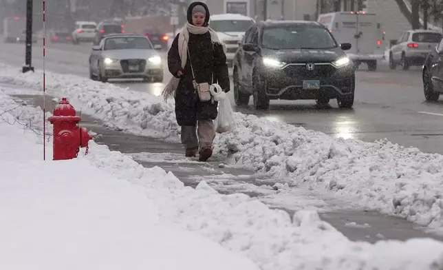 A pedestrian walks on a snow-covered sidewalk in Wheeling, Ill., Monday, Dec. 1, 2025. (AP Photo/Nam Y. Huh)