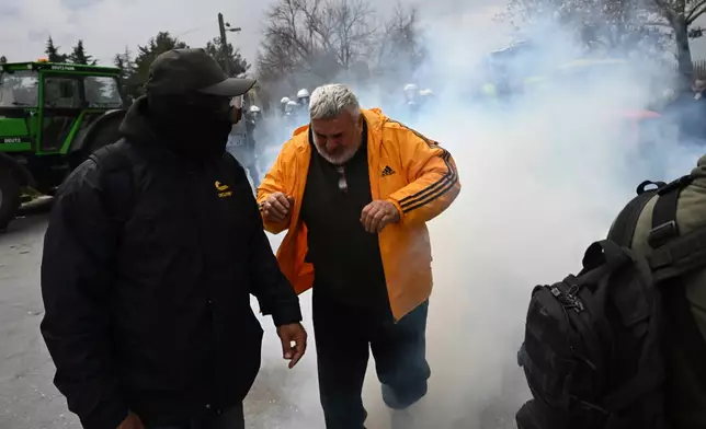 A man runs to avoid tear gas during clashes with riot police after farmers tried to block the main access road to Thessaloniki's international airport, northern Greece, on Friday, Dec. 5, 2025, as protests over delays in European Union-backed agricultural subsidy payments escalated. (AP Photo/Giannis Papanikos)