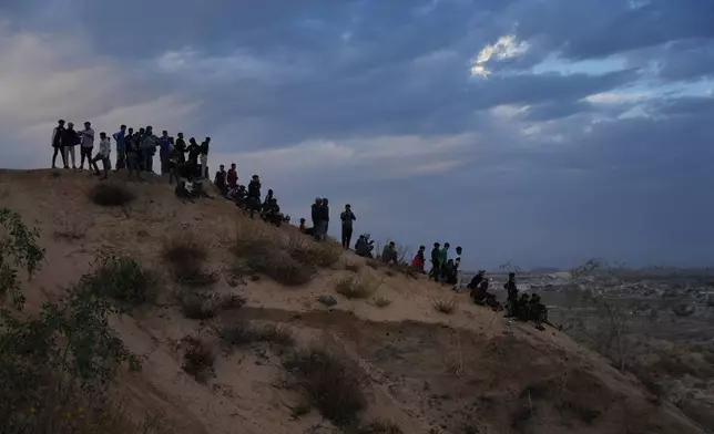 Palestinians watch youths riding their motorcycles on sand dunes in the Al-Zahra area, in the central Gaza Strip, Friday, Dec. 5, 2025. (AP Photo/Abdel Kareem Hana)