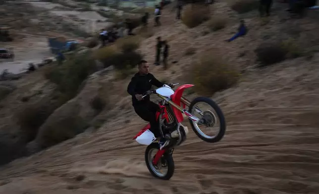 A Palestinian man rides his motorcycle on a sand dune in the Al-Zahra area, in the central Gaza Strip, Friday, Dec. 5, 2025. (AP Photo/Abdel Kareem Hana)