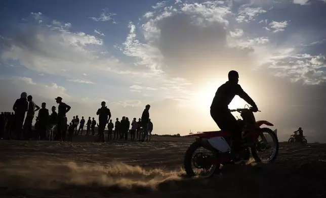 Palestinians watch youths riding their motorcycles on a sand dune in the Al-Zahra area, in the central Gaza Strip, Friday, Dec. 5, 2025. (AP Photo/Abdel Kareem Hana)