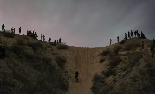 Palestinians watch youths riding their motorcycles on sand dunes in the Al-Zahra area, in the central Gaza Strip, Friday, Dec. 5, 2025. (AP Photo/Abdel Kareem Hana)