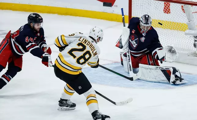 Winnipeg Jets' Josh Morrissey (44) defends against Boston Bruins' Elias Lindholm (28) as he scores on goaltender Eric Comrie (1) during the third period of an NHL hockey game, in Winnipeg, Manitoba, Thursday, Dec. 11, 2025. (John Woods/The Canadian Press via AP)