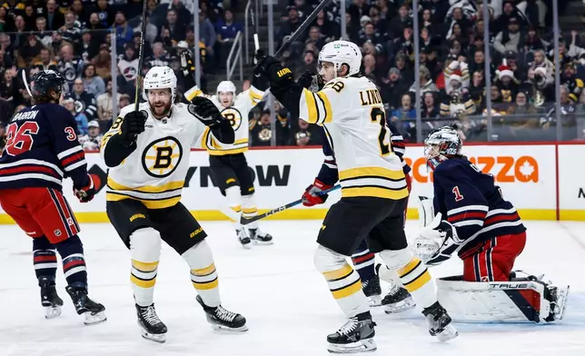 Boston Bruins' Elias Lindholm (28) and Pavel Zacha (18) celebrate David Pastrnak's goal against Winnipeg Jets goaltender Eric Comrie (1) during the first period of an NHL hockey game in Winnipeg, Manitoba, Thursday, Dec. 11, 2025. (John Woods/The Canadian Press via AP)