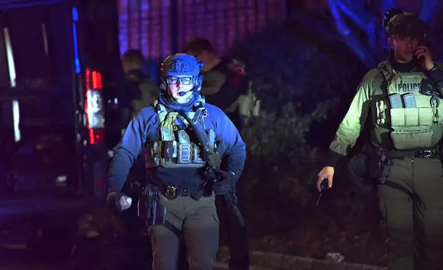 A law enforcement official carries a rifle in a neighborhood near Brown University, Saturday, Dec. 13, 2025, in Providence, R.I. during the investigation of a shooting. (AP Photo/Steven Senne)