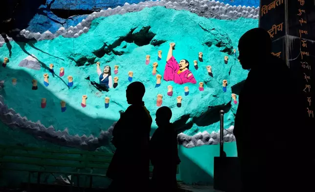 Tibetan monks are silhouetted as they walk past a mural at the Tsuglakhang temple in Mcleodganj near Dharamshala, India, March 6, 2025. (AP Photo/Manish Swarup)