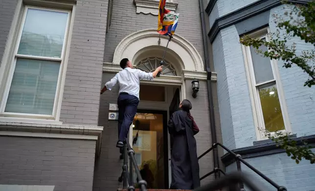 Namkyi, right, a Tibetan former political prisoner who was arrested at 15 for protesting Chinese rule, watches as Tsultrim Gyatso, China Director at Office of Tibet, untangles the Tibetan flag over the office entrance in Washington, Oct. 9, 2025. (AP Photo/David Goldman)