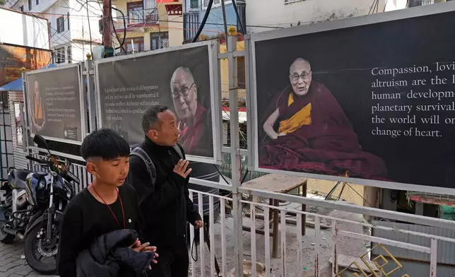 Sonam Tashi, right, and his son, Kunga Tenzin, pass photographs of Tibetan spiritual leader Dalai Lama at the entrance of the Tsuglakhang temple in Mcleodganj near Dharamshala, India, March 6, 2025. (AP Photo/Manish Swarup)