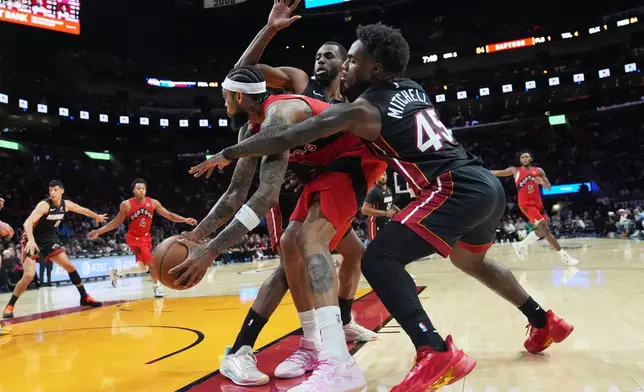 Miami Heat forward Andrew Wiggins, left, and guard Davion Mitchell (45) defend Toronto Raptors forward Brandon Ingram, center, during the second half of an NBA basketball game, Monday, Dec. 15, 2025, in Miami. (AP Photo/Lynne Sladky)