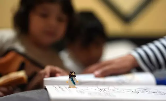 A miniature Jesus figurine sits on a coloring book inside the Miami-area motel room where Jakelin Pasedo is living with her two sons, who all have refugee status, Wednesday, Oct. 22, 2025, after their father requested to be sent back to Venezuela after months in immigration detention. (AP Photo/Rebecca Blackwell)