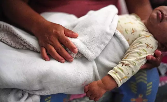 Guatemalan migrant Amavilia, 31, holds her infant son, whose father Edgar was detained days after his birth and later deported to Guatemala, inside the South Florida apartment where she lives with her two children and a roommate, Wednesday, Oct. 8, 2025. (AP Photo/Rebecca Blackwell)